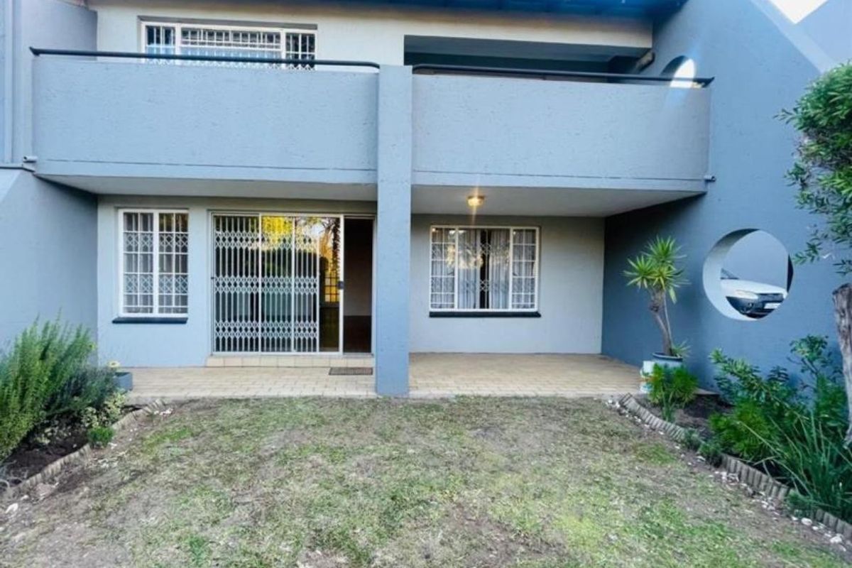 Rear view of the apartment featuring a covered ground-floor patio, an upper-level balcony, and a small private garden area.