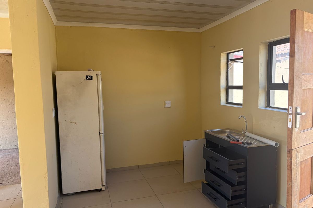A compact kitchen area featuring tiled flooring, a stainless steel sink unit, and basic cabinetry, offering a functional space ready for updates.