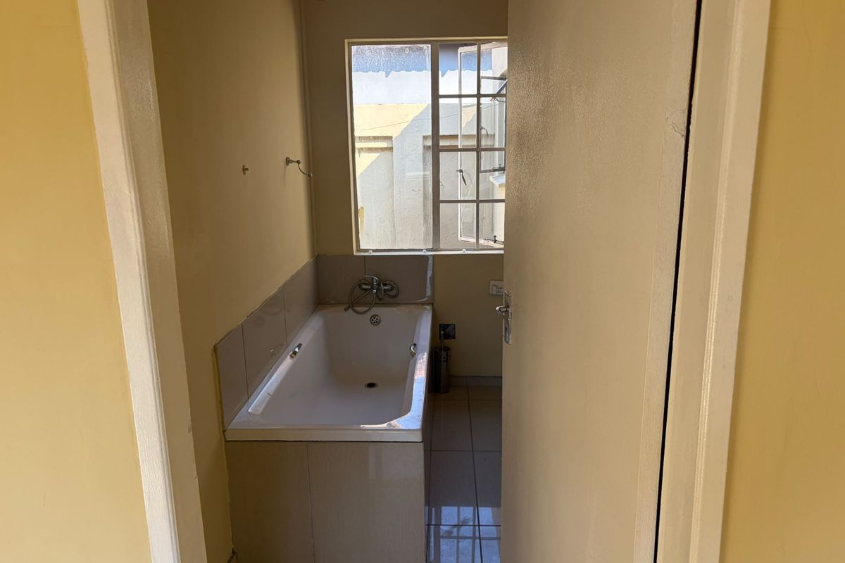 A compact bathroom featuring a built-in bathtub with tiled splashback and tiled flooring, requiring some cosmetic updates.