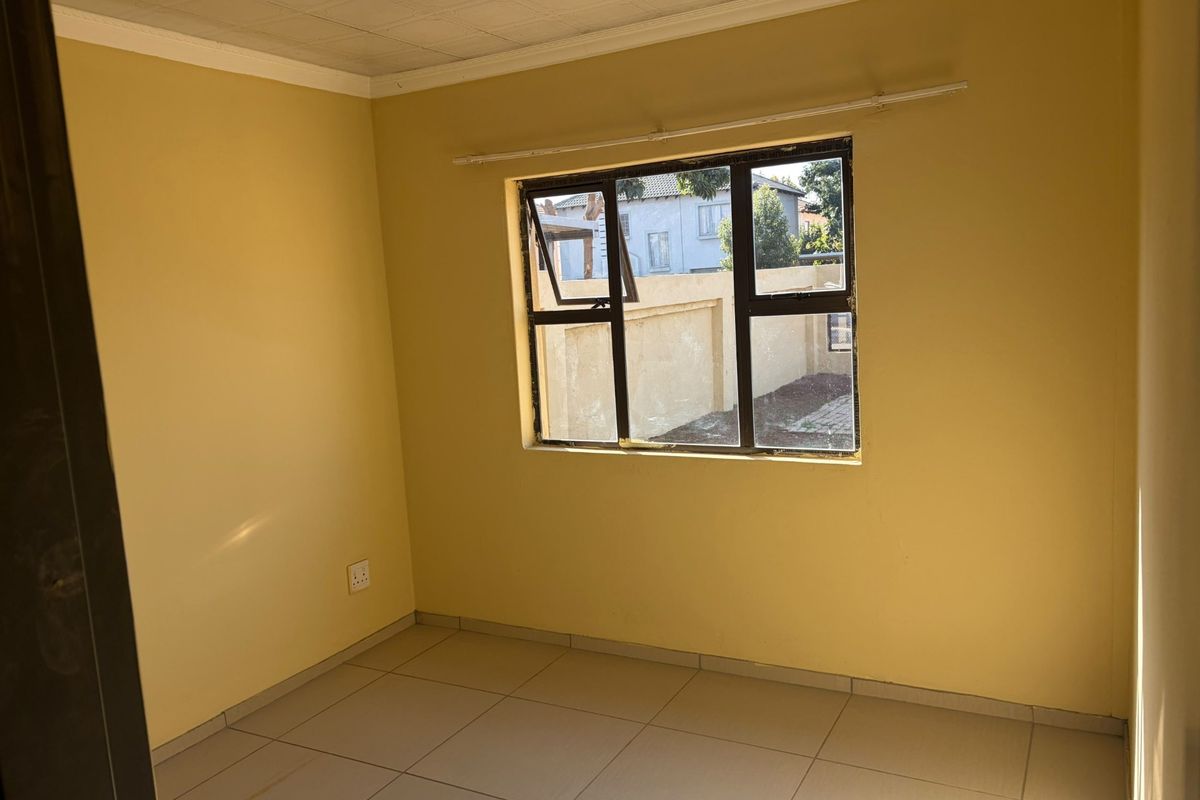 An empty bedroom featuring tiled flooring, yellow walls, and a metal-framed window. The space is ready for renovation or staging.