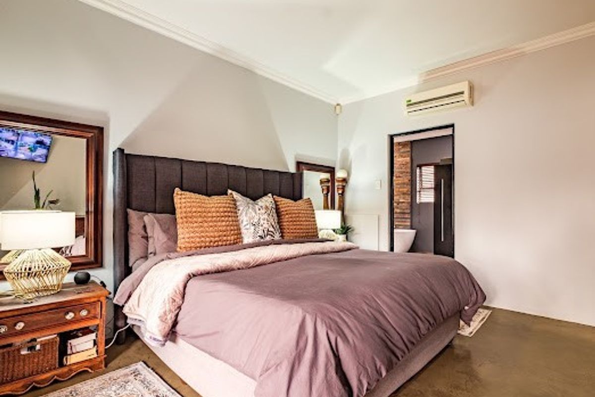 A well-maintained bedroom featuring polished concrete floors, crown molding, and a wall-mounted split-system air conditioner, with an adjoining ensuite bathroom.