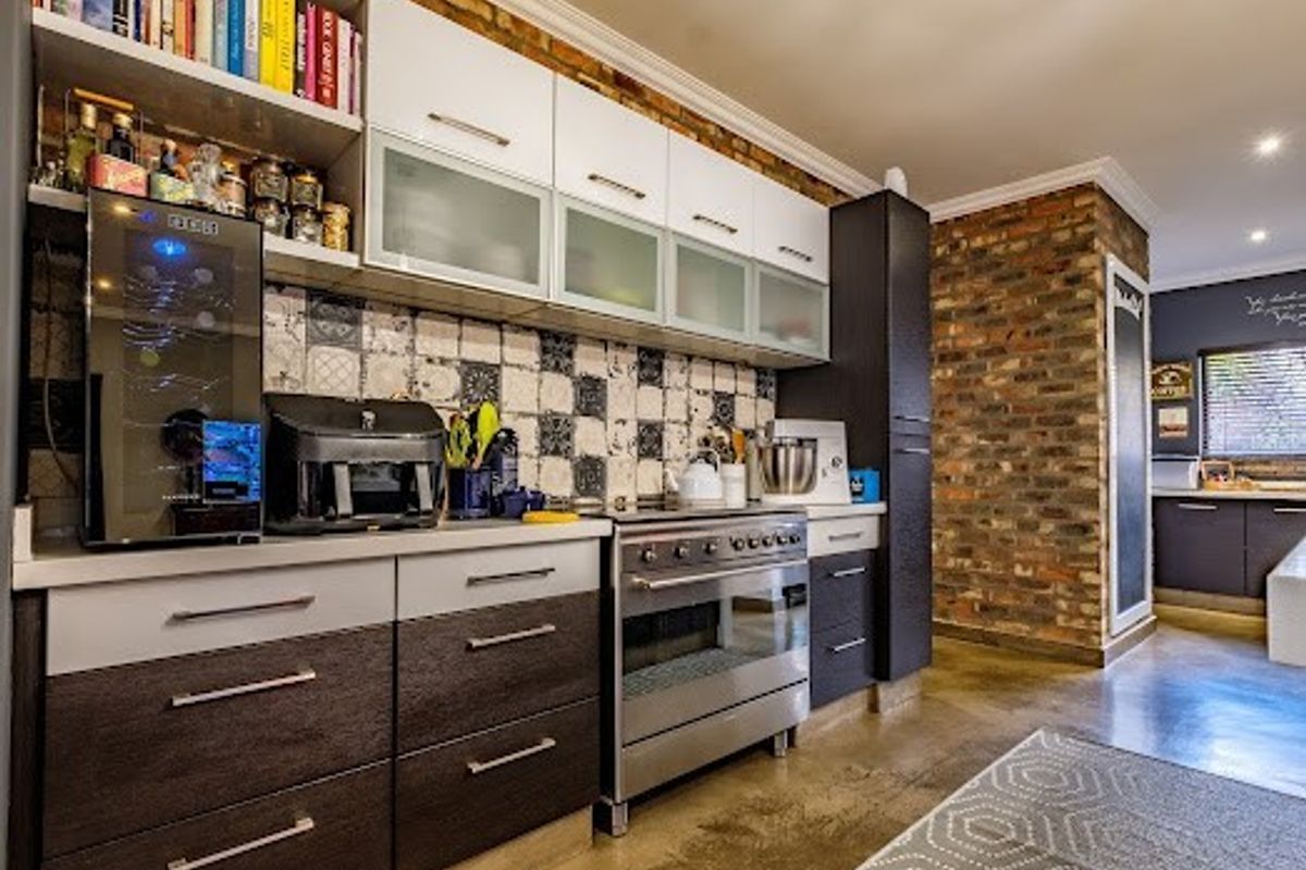 Modern kitchen featuring dark and white cabinetry, a stainless steel oven, patterned tile backsplash, and an exposed brick feature wall with polished concrete floors.