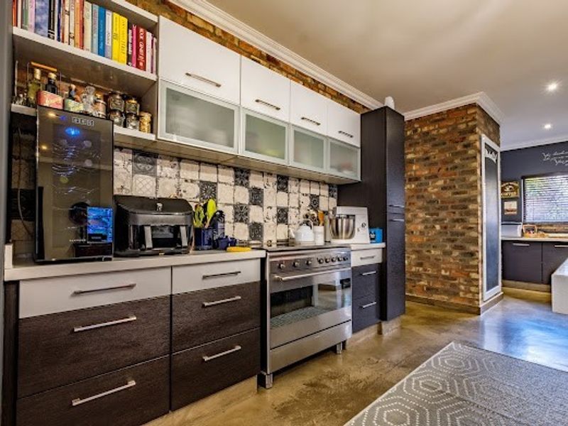 Modern kitchen featuring dark and white cabinetry, a stainless steel oven, patterned tile backsplash, and an exposed brick feature wall with polished concrete floors.