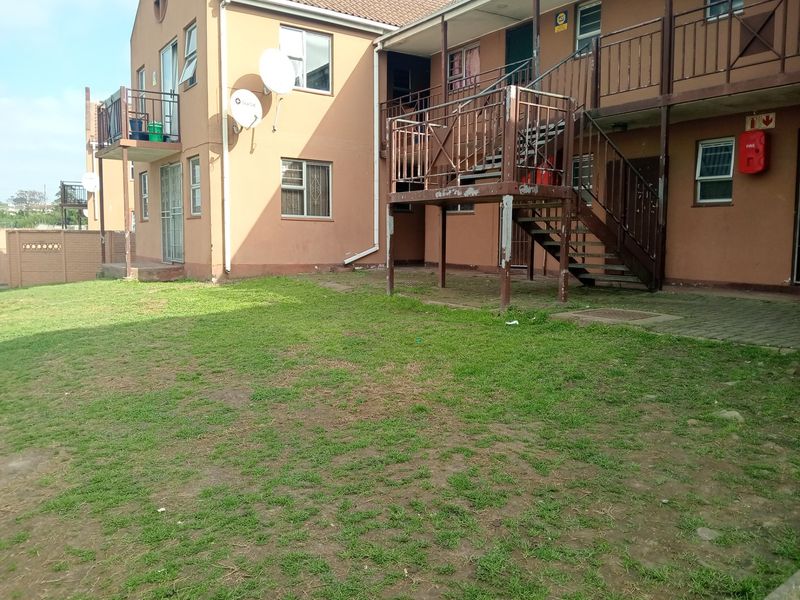 Rear view of an apartment complex featuring a communal lawn area, metal staircase access, and exterior building finishes.
