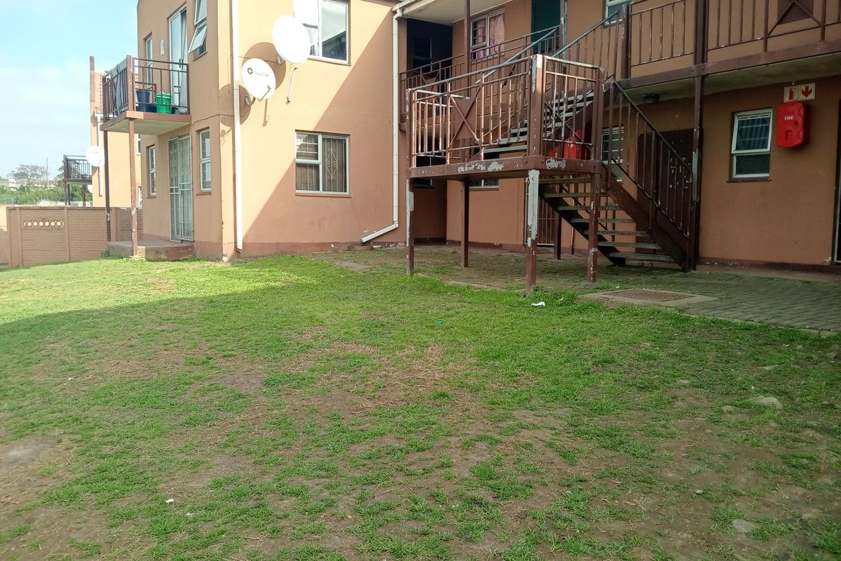 Rear view of an apartment complex featuring a communal lawn area, metal staircase access, and exterior building finishes.