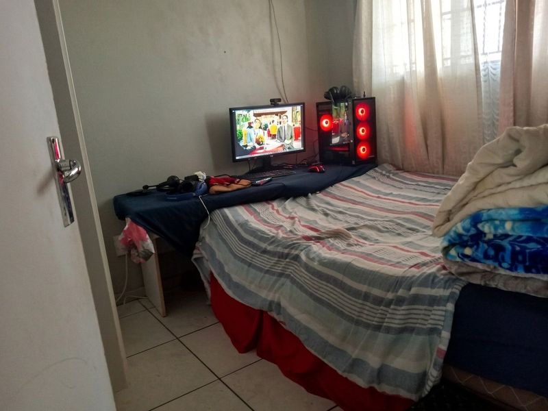 A compact bedroom featuring tiled flooring and a window with natural light, currently utilized as a multi-purpose living and sleeping space.