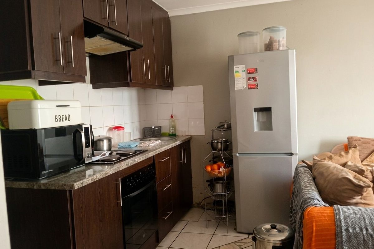 Compact kitchen featuring dark wood cabinetry, granite countertops, built-in oven, and electric hob with an extractor fan.