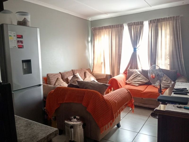 A living room area featuring tiled flooring and cove cornicing, currently furnished with seating and window treatments.