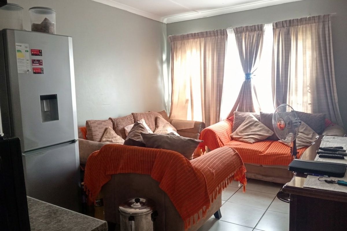 A living room area featuring tiled flooring and cove cornicing, currently furnished with seating and window treatments.
