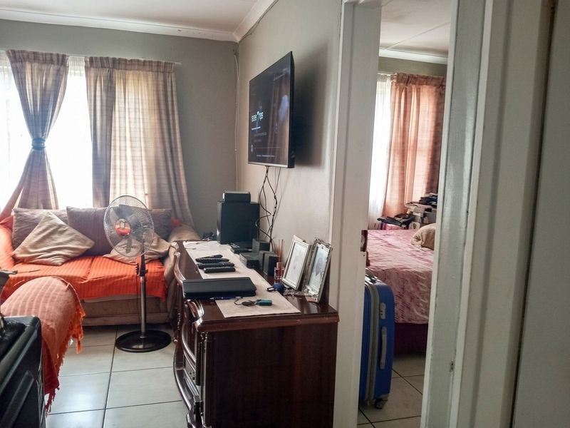 A living room area featuring tiled flooring and a wall-mounted television, with an adjacent view into a bedroom space.