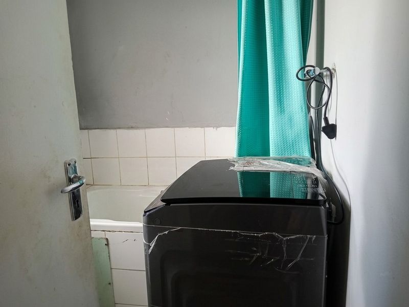 A small laundry area featuring a bathtub and tiled splashback, currently used for utility purposes.
