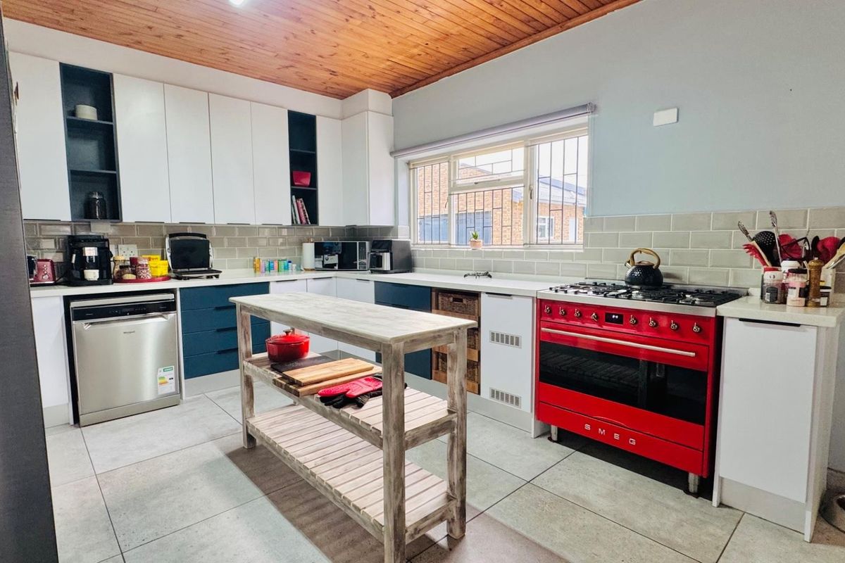 A well-lit kitchen featuring modern white and blue cabinetry, a striking red gas stove, subway tile backsplash, and a warm timber ceiling.