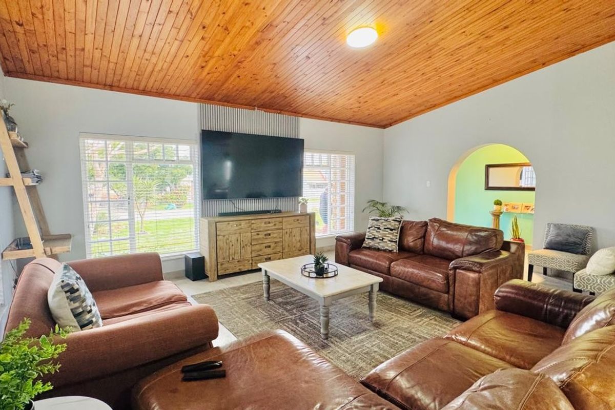 Spacious living room featuring a warm timber-clad vaulted ceiling, large windows for natural light, and a distinctive vertical slat feature wall.