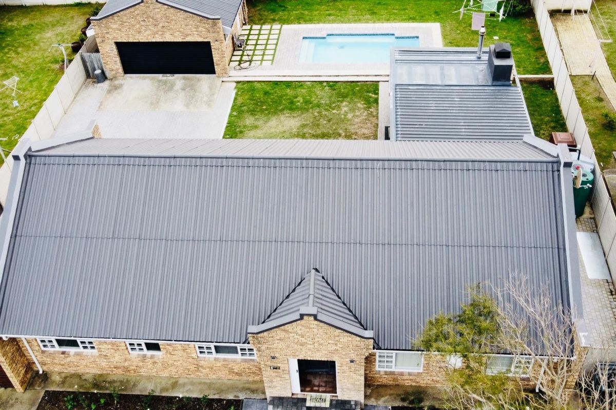 Aerial view of the property featuring a corrugated metal roof, a swimming pool, a detached garage, and a well-maintained brick exterior.