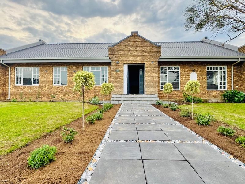 A well-maintained single-story face brick home featuring a metal roof, a central entrance, and a neatly paved walkway leading through a landscaped front garden.