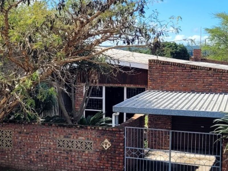 Front view of a brick house featuring a paved driveway, metal gate, and a covered carport area.