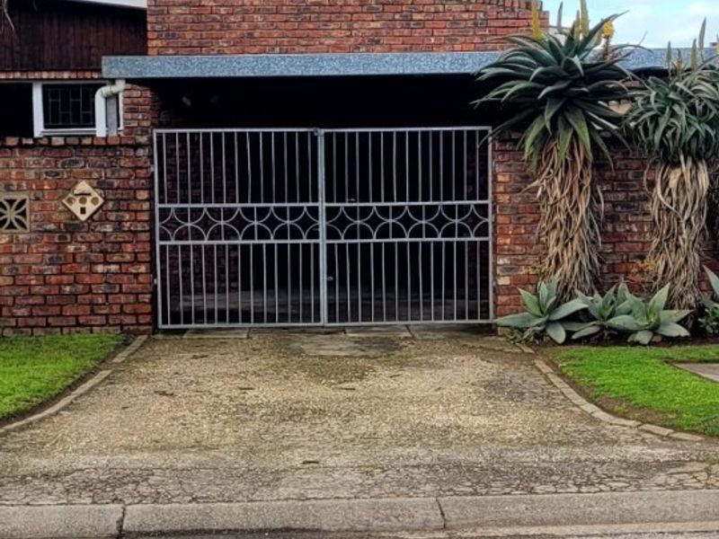 Front exterior view featuring a brick facade, a metal driveway gate, and a covered carport area with a concrete driveway.