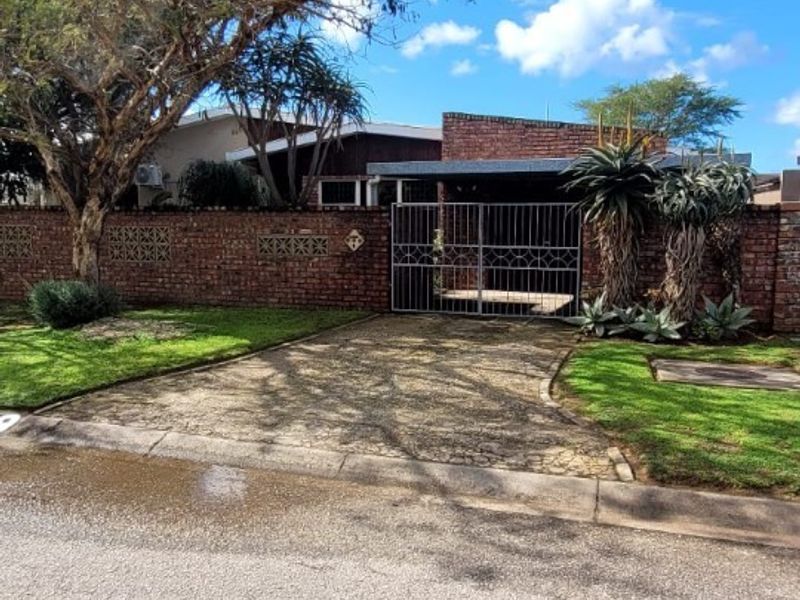 Front view of the property featuring a brick boundary wall, metal driveway gate, and a paved driveway leading to the entrance.