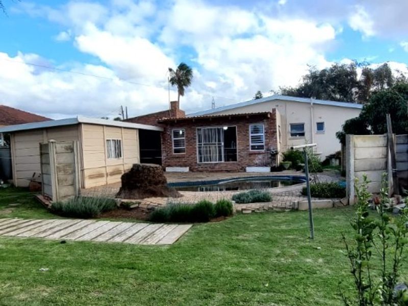 Rear view of the property featuring a swimming pool, paved patio area, and a spacious garden with boundary walling.