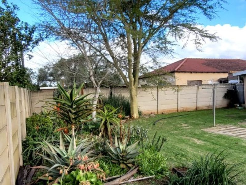 A private rear garden featuring a lawn, mature tree, and established garden beds enclosed by a precast concrete boundary wall.