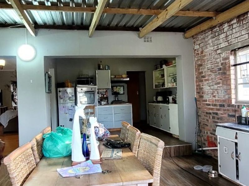 Open-plan living and dining area featuring exposed brickwork, timber rafters, corrugated metal roofing, and a functional kitchen with built-in appliances.