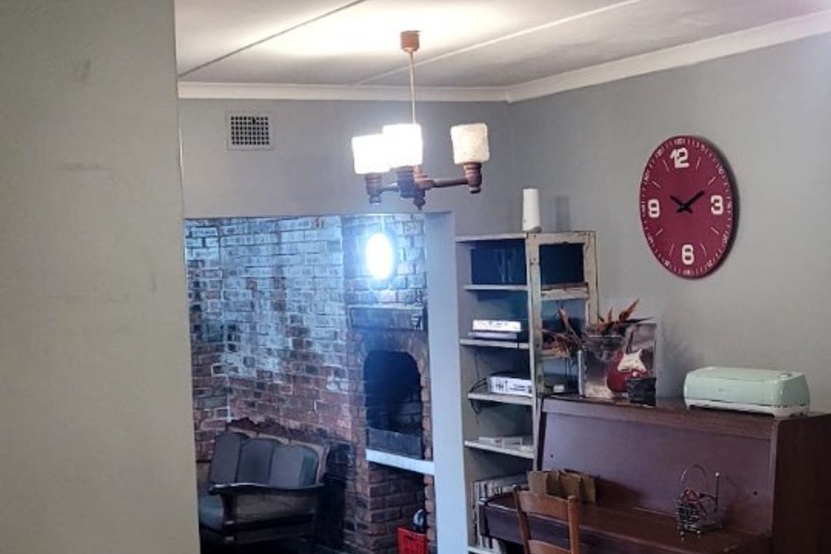 A living room featuring hardwood flooring, a brick fireplace in the adjacent area, and a ceiling fan.