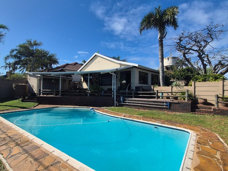 Rear garden area featuring a swimming pool, stone paved surround, brick retaining walls, and a covered patio attached to the main house.