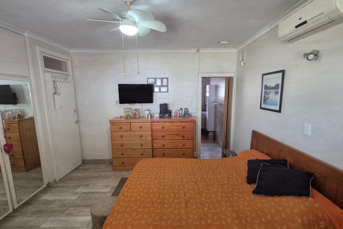 A functional bedroom featuring built-in mirrored wardrobes, tiled flooring, a ceiling fan, and a wall-mounted air conditioning unit.
