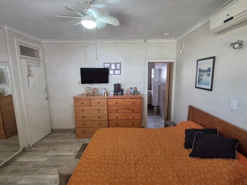 A functional bedroom featuring built-in mirrored wardrobes, tiled flooring, a ceiling fan, and a wall-mounted air conditioning unit.