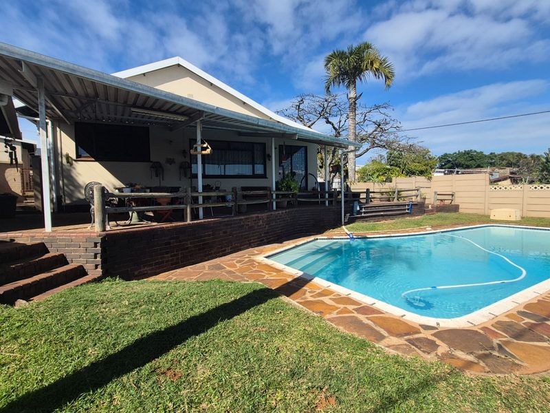 Rear exterior view featuring a swimming pool with paved surround, a covered patio area, and a brick retaining wall.