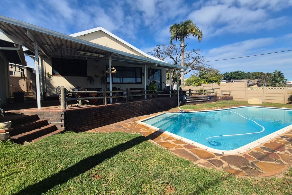 Rear exterior view featuring a swimming pool with paved surround, a covered patio area, and a brick retaining wall.