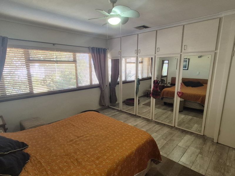 Spacious bedroom featuring extensive built-in mirrored wardrobes, tiled flooring, and a ceiling fan, offering ample storage and natural light.