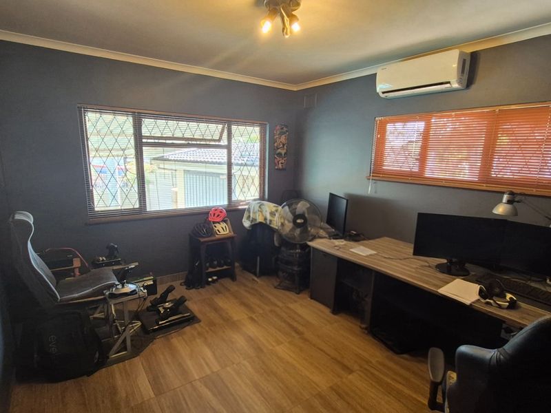 A functional home office space featuring laminate flooring, a wall-mounted split-system air conditioner, and security bars on the windows.
