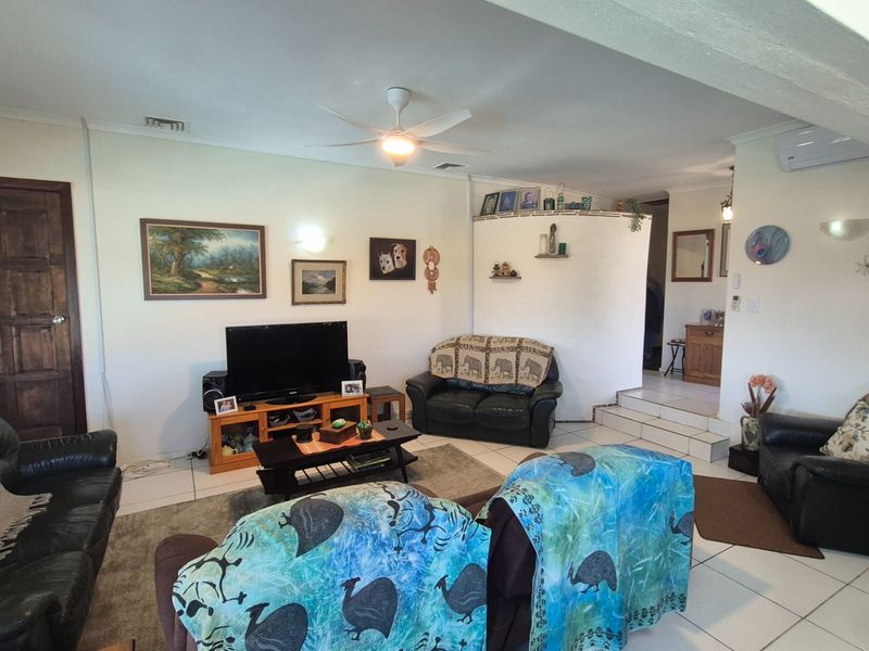 Spacious living room featuring tiled flooring, a ceiling fan, and a split system air conditioner, with a raised platform area leading to other rooms.