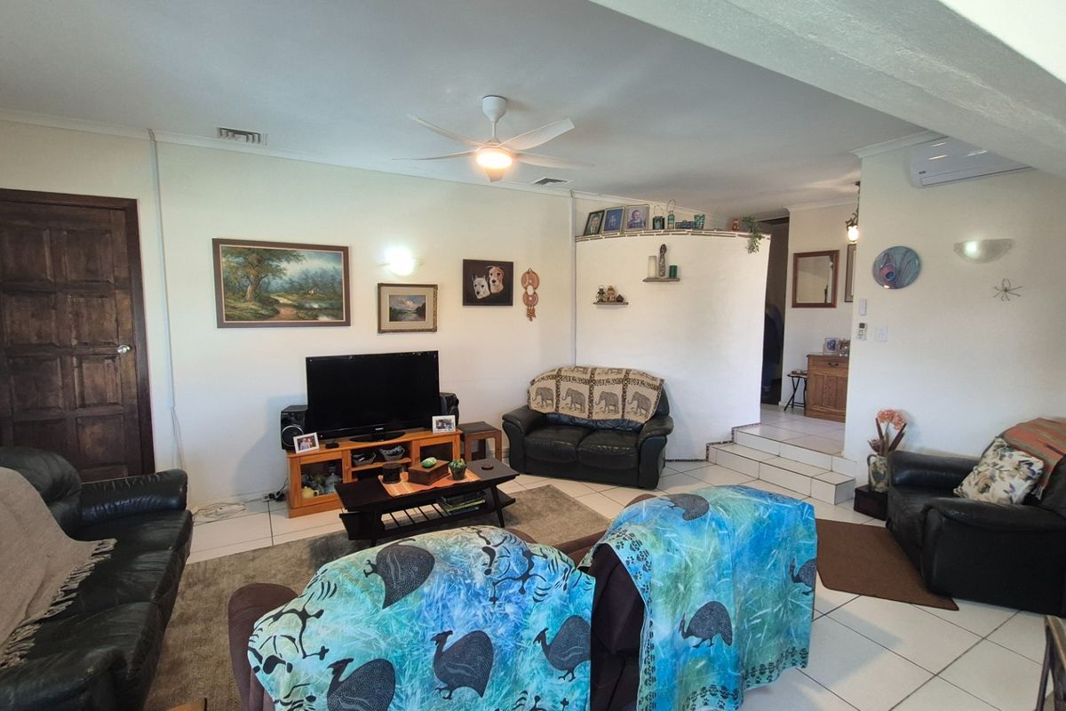 Spacious living room featuring tiled flooring, a ceiling fan, and a split system air conditioner, with a raised platform area leading to other rooms.