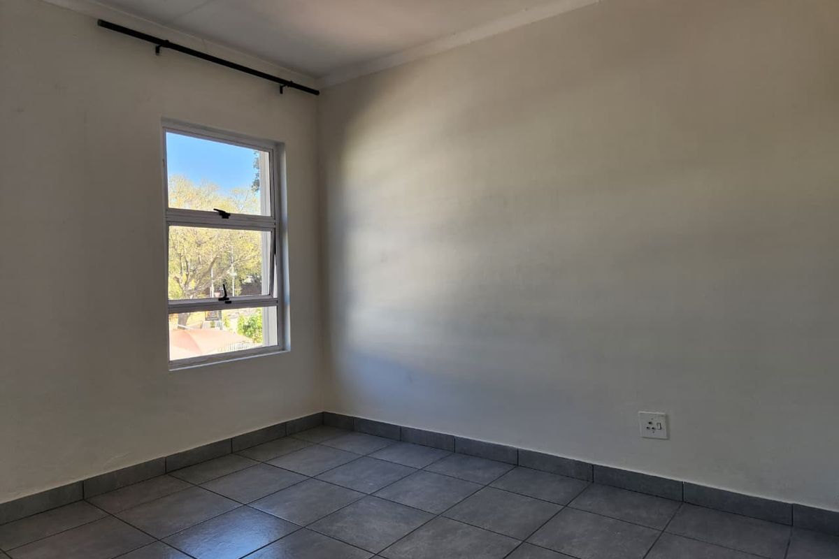 A vacant bedroom featuring neutral tiled flooring, a single window with a curtain rod, and standard electrical outlets.