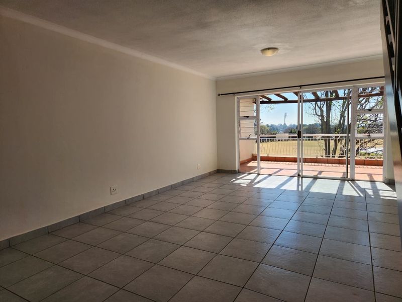 An empty, tiled living room featuring a large sliding glass door that opens onto a balcony with outdoor views.