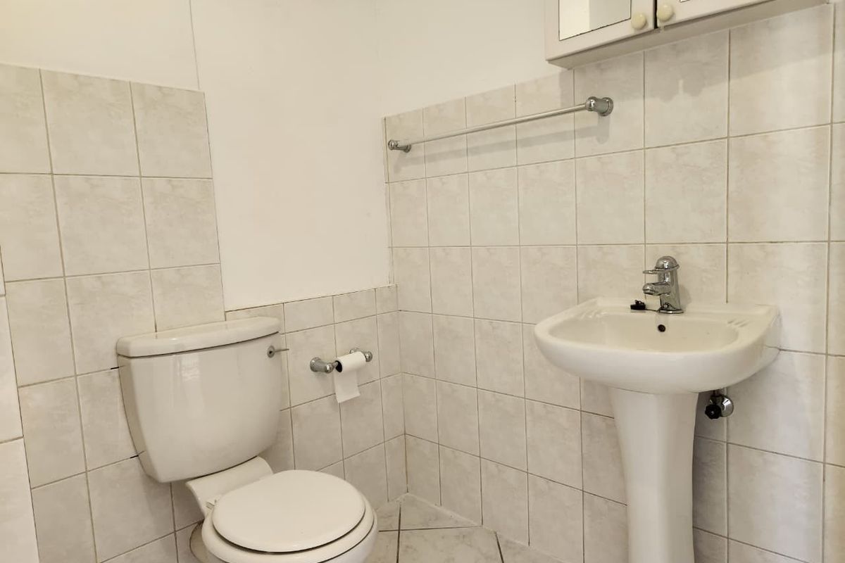 A compact bathroom featuring a pedestal basin, toilet, and tiled finishes, offering a functional space ready for modernization.