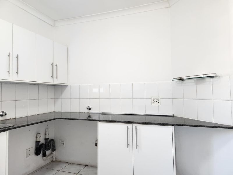 A functional kitchen area featuring white cabinetry, granite countertops, and tiled backsplash, with dedicated plumbing connections for appliances.