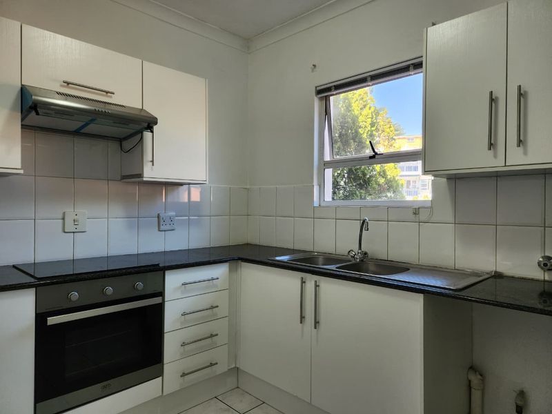 A functional kitchen featuring white cabinetry, granite countertops, a built-in oven, electric hob, extractor fan, and a double sink with tiled backsplash.