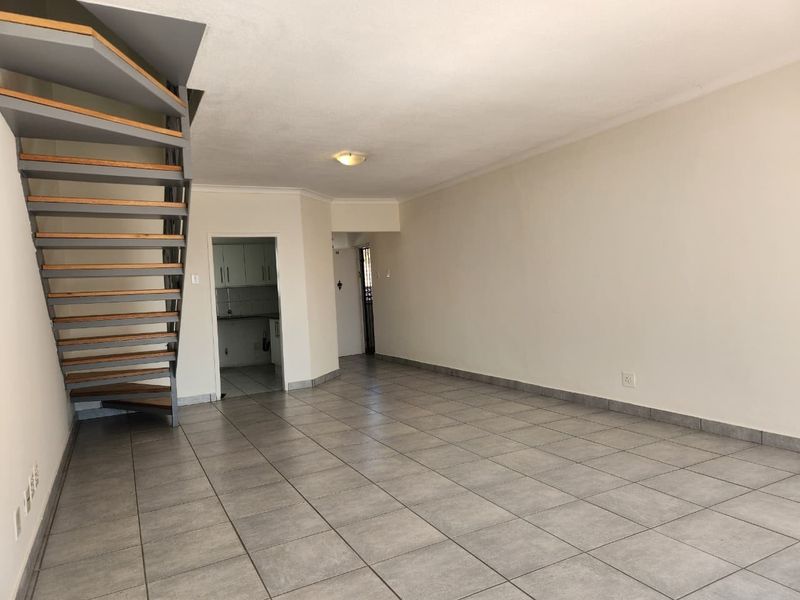 An open-plan living area featuring neutral tiled flooring, a modern spiral staircase, and direct access to a kitchen space.