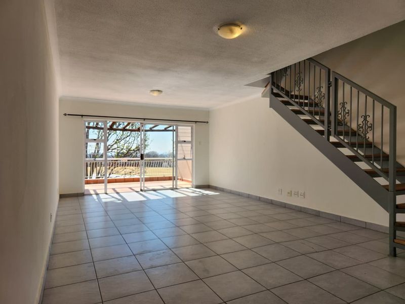 Spacious open-plan living area featuring tiled flooring, a staircase with a metal balustrade, and sliding glass doors leading to an outdoor patio.