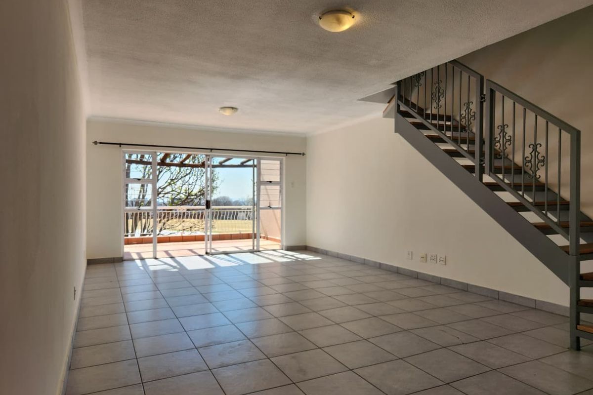 Spacious open-plan living area featuring tiled flooring, a staircase with a metal balustrade, and sliding glass doors leading to an outdoor patio.