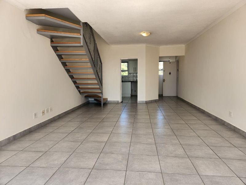 Spacious open-plan living area featuring neutral tiled flooring and a modern staircase with a metal balustrade, leading to a separate kitchen area.