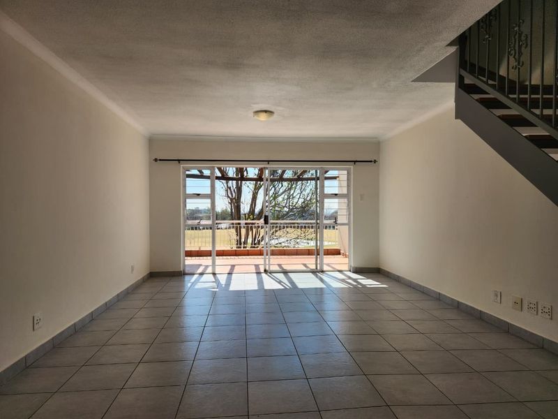 An empty, open-plan living area featuring neutral tiled flooring, a staircase, and large sliding glass doors leading to an outdoor balcony.