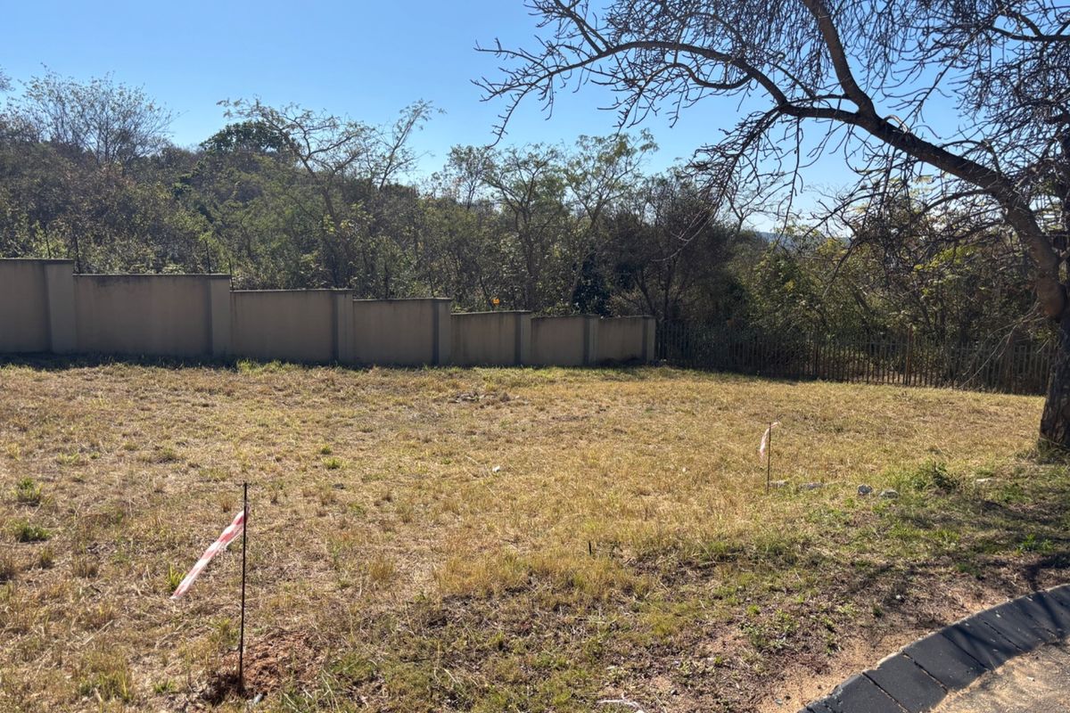 A vacant residential plot featuring a boundary wall and perimeter fencing, surrounded by established trees and natural vegetation.
