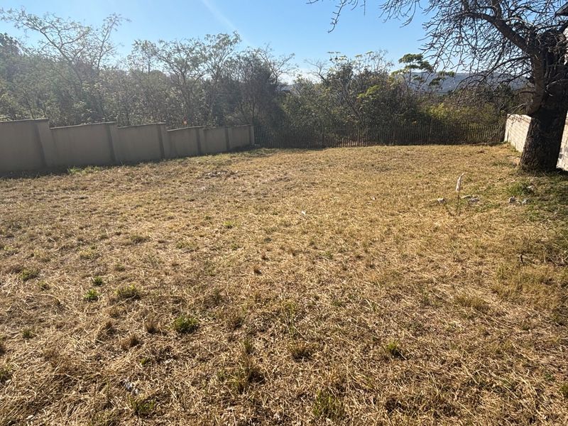 A vacant residential plot featuring a level grassed area enclosed by perimeter walls and fencing, offering a blank canvas for development.