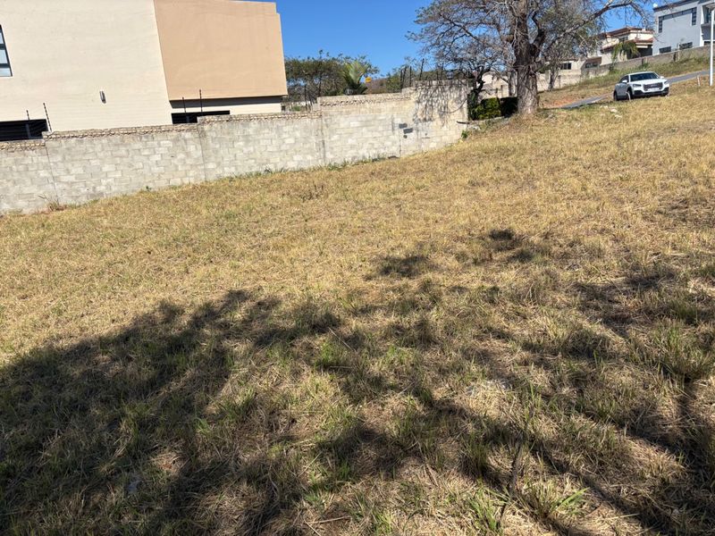 A vacant residential plot featuring dry grass, a perimeter boundary wall, and installed electric fencing.