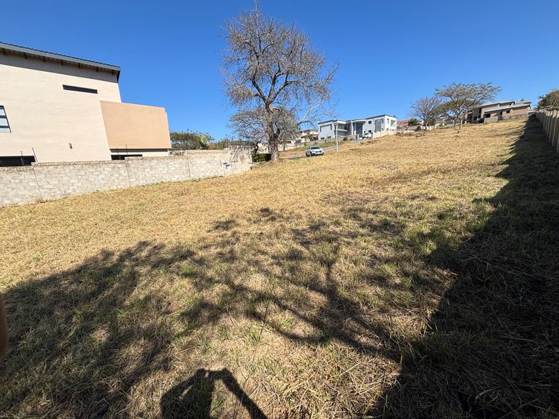 A vacant residential plot featuring a gentle slope, enclosed by boundary walls, situated in a developed neighborhood.