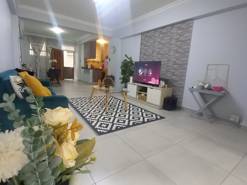 Open-plan living area featuring tiled floors, a stone-cladding feature wall, and recessed ceiling lighting, creating a bright and connected living space.
